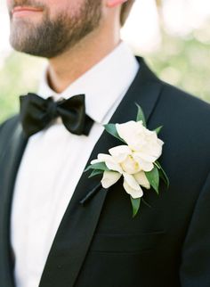 a man in a tuxedo with a white flower on his lapel and black bow tie