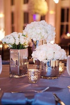 white flowers in silver vases on a table at a wedding reception with candles and napkins