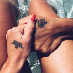 two people with tattoos on their legs sitting in the water and holding each other's hands