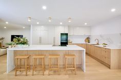 a kitchen with white counter tops and wooden stools next to an island in the middle