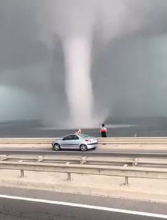 a car driving down a highway under a large tornado