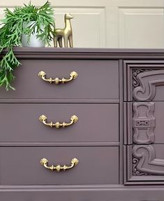 a purple dresser with gold handles and knobs next to a potted green plant