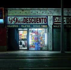 an empty street at night in front of a store with its doors open and the lights on