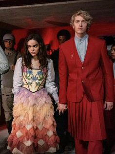 two people dressed in red and pink standing next to each other with others looking on