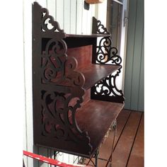 an old wooden shelf with wrought iron designs on it's sides, sitting in front of a white building