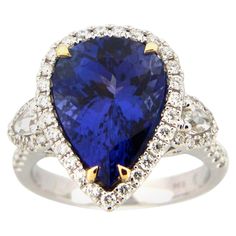 This stunning cocktail ring showcases a beautiful 5.94 Carat Pear Shape Tanzanite with a Diamond Halo. The Tanzanite is flanked by two Rose Cut White Diamonds, and sits on a Diamond Shank. This ring is set in 18k White Gold, with 18k Yellow Gold prongs on the Tanzanite. Total Diamond Weight = 0.64 carats. Ring Size is 6 1/2. Elegant Pear-shaped Sapphire Ring For Formal Occasions, Elegant Formal Pear-shaped Sapphire Ring, Elegant Multi-stone Pear-shaped Diamond Ring, Formal Teardrop Ring Gia Certified, Elegant Gia Certified Pear-shaped Sapphire Ring, Elegant Gia Certified Pear-shaped Ring, Elegant Pear-shaped Gia Certified Ring, Gia Certified Pear-shaped Ring For Formal Occasions, Gia Certified Pear Shaped Ring For Formal Occasions