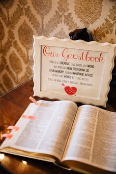 an open book sitting on top of a wooden table next to a sign that says our guestbook