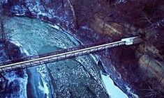 an aerial view of a bridge over a river in the woods with snow on the ground