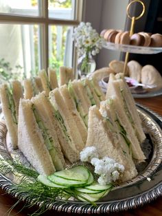 a platter filled with sandwiches and cucumbers on top of a wooden table