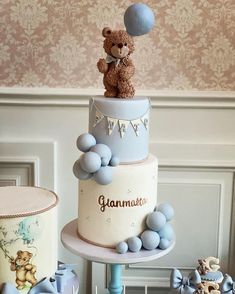 a teddy bear sitting on top of a three tiered cake with blue balls around it