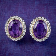 A glamorous pair of antique Victorian cluster earrings built around two regal purple amethysts (approx. 5ct each) bezel set in the centre of a halo of twinkling old mine cut diamonds (approx. 2ct total). Amethyst is considered a stone of protection, clarity and tranquillity and has been highly esteemed throughout the ages for its stunning beauty and deep violet colouring which has adorned regal jewellery all around the world, from ancient Egypt to the British crown jewels. The pair is a union of Formal Purple Diamond Earrings, Luxury Purple Earrings For Anniversary, Vintage Oval Diamond Earrings For Formal Occasions, Formal Purple Amethyst Ring With Rose Cut Diamonds, Elegant Purple Clip-on Earrings, Formal Purple Round Earrings, Luxury Purple Round Earrings, Formal Purple Clip-on Jewelry, Purple Oval Fine Jewelry Earrings