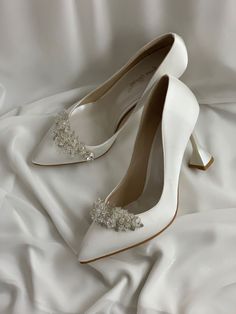 white wedding shoes with pearls on the toe and heel are sitting on a bed sheet