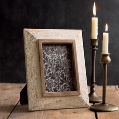 an old photo frame and two candles are sitting on a wooden table next to each other