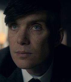 a close up of a person wearing a suit and tie with blue eyes in the dark