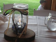 a mason jar filled with water sitting on top of a wooden slice next to a candle