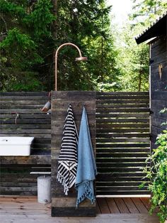 an outdoor shower with towels hanging on the wall and a sink next to it in front of a wooden fence