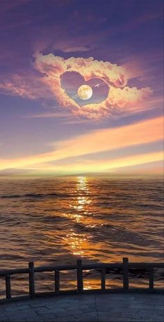 a heart shaped object floating in the air over water at sunset or sunrise with clouds