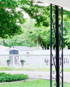 an open door in front of a white picket fence with trees and bushes behind it