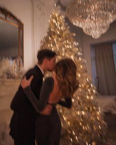 a man and woman are kissing in front of a christmas tree with lights on it