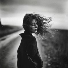 a woman standing on the side of a road with her hair blowing in the wind