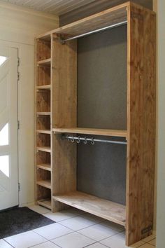 an empty wooden closet with shelves and hooks on the door handlebars, in front of a white wall