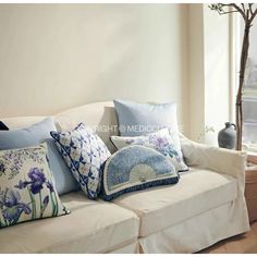 a white couch with pillows on it in front of a window and a vase filled with flowers