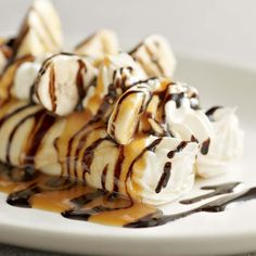 a white plate topped with banana split covered in chocolate sauce and drizzled with ice cream