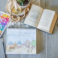 an open book sitting on top of a wooden table next to a potted plant