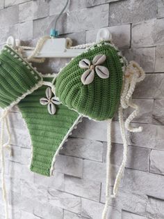 two green knitted hats hanging on a brick wall next to a white hook with buttons