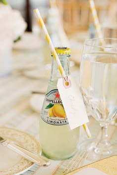 a bottle of lemonade sitting on top of a table next to two wine glasses