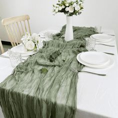 the table is set with white plates and flowers in a vase on top of it