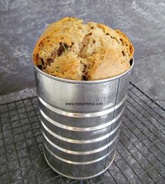 a muffin in a metal bucket sitting on top of a wire rack next to a wall