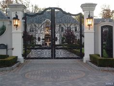 an iron gate in front of a house with two lamps on either side of it