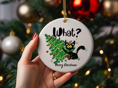 a hand holding a christmas ornament with a black cat on it