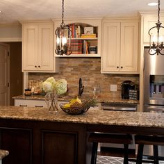 a kitchen with white cabinets and marble counter tops, two vases filled with flowers on the island