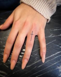 a person's hand with a small cross tattoo on the middle of their finger