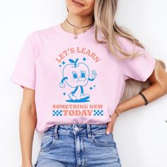 This super-soft Comfort Colors® Retro Teacher Shirt features a cute apple mascot design, and the phrase Let's Learn Something New Today. Printed on Comfort Colors® tees for that vintage, lived-in feel and look - easy to style oversized or wear as a relaxed fit tee. Please check the size charts for the perfect fit! Details: ✔100% Ethically grown cotton ✔ Mediumweight fabric - durable and soft ✔ Premium DTG prints - no peeling or cracking ✔ Relaxed fit: Drapes effortlessly on any body type. ✔ Easy Cute Tops With Funny Text For Back To School, Pink Slogan T-shirt For School, Funny Cartoon Print T-shirt For School, Pink Relaxed Fit T-shirt For School, Funny Crew Neck Tops For Back To School, Cute Slogan T-shirt For Back To School, Back To School Funny Text Short Sleeve T-shirt, Trendy Short Sleeve T-shirt For Back To School, Funny Short Sleeve T-shirt For Back To School