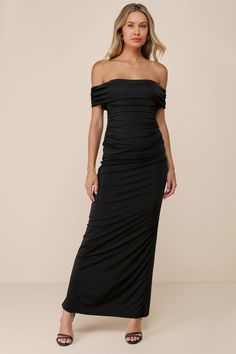 a woman wearing a black dress with off the shoulder and side slits, standing in front of a white background