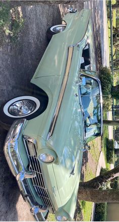 an old green car is parked on the side of the road in front of a tree