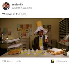 a man in a suit and yellow tie sitting at a desk wearing a paper hat