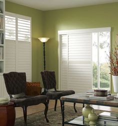 a living room with two chairs and a table in front of the window that has shutters open