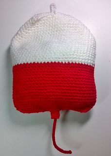 a red and white knitted hat hanging from a hook on the side of a wall