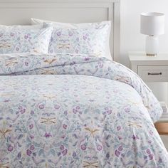 a bed with white and blue floral bedspread on top of it next to a night stand