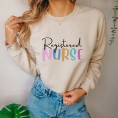 a woman wearing a white sweatshirt with the words restored nurse printed on it in multicolored letters