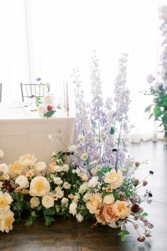 flowers and greenery are arranged on the floor in front of a white table cloth