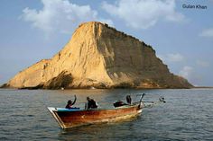 two people in a boat on the water near a large rock outcropping