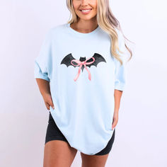 Get ready to swoon over our Black Bat Pink Bow T-Shirt, a perfect blend of spooky and cute for your Halloween festivities! Featuring an adorable black bat design with a charming pink bow, this t-shirt is sure to be a hit whether you're attending a Halloween party, heading to a pumpkin patch, or just getting into the spirit of the season. Made from 100% ring-spun cotton, this tee offers a soft-washed, garment-dyed fabric that delivers exceptional coziness. Spooky Cotton Top For Costume Party, Spooky Cotton Tops For Costume Party, Spooky Character Print Tops For Costume Party, Cute Halloween Tops With Character Print, Cute Halloween Short Sleeve Tops, Cute Short Sleeve Halloween Tops, Cute Short Sleeve Tops For Halloween, Cotton Crew Neck Top For Costume Party, Casual Short Sleeve Tops For Costume Party