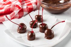 chocolate covered cherries are sitting on a white plate next to a red and white checkered napkin