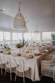 a dining room table set with white chairs and place settings in front of large windows