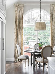 a dining room table with chairs and a lamp hanging from the ceiling in front of an arched window